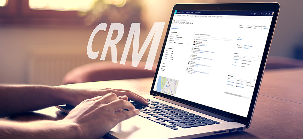 Eine Person benutzt einen Laptop, auf dem eine CRM- (Customer Relationship Management) und ERP-Softwareoberfläche angezeigt wird, wobei die Buchstaben CRM digital in großer, transparenter Schrift neben dem Bildschirm eingeblendet sind.