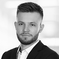 Schwarz-Weiß-Porträt eines jungen Mannes mit kurzem Haar und gestutztem Bart, der eine Anzugsjacke und ein Hemd mit Kragen trägt und selbstbewusst in die Kamera blickt - perfekt für ein professionelles ERP-Profil vor einem unscharfen Hintergrund.