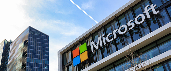 microsoft-gebäude Modernes Bürogebäude mit dem Microsoft-Logo und bunten Fenstersymbolen an der Fassade vor blauem Himmel. Im Hintergrund ist ein weiteres gläsernes Hochhaus zu sehen.