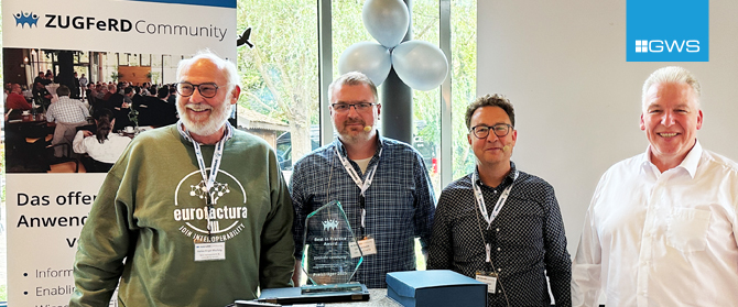 Vier lächelnde Männer stehen drinnen bei den ZUGFeRD-Entwicklertagen 2025, einer hält eine Auszeichnung in der Hand. Hinter ihnen ein ZUGFeRD-Gemeinschaftsbanner in deutscher Sprache, ein Fenster mit Bäumen draußen, Luftballons und das GWS-Logo in der oberen rechten Ecke.