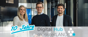 Drei Personen, zwei Männer und eine Frau, stehen in einem Haus und lächeln in die Kamera. Eine Grafik überlagert die Worte 10 Jahre und Digital Hub münsterLAND mit einem blau-weißen Sechseck-Logo.