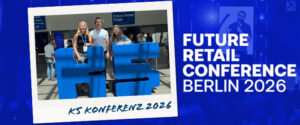 Drei Personen stehen lächelnd hinter einer großen blauen K5-Skulptur bei einer Veranstaltung. Der Text lautet: „FUTURE RETAIL CONFERENCE BERLIN 2026“ und „K5 KONFERENZ 2026“. Im Hintergrund ist das Schild „Future Retail Stage“ zu sehen.