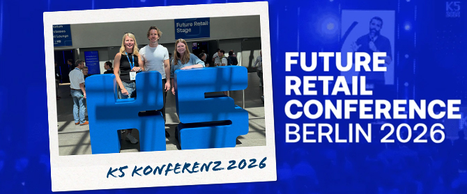 Drei Personen stehen lächelnd hinter einer großen blauen K5-Skulptur bei einer Veranstaltung. Der Text lautet: „FUTURE RETAIL CONFERENCE BERLIN 2026“ und „K5 KONFERENZ 2026“. Im Hintergrund ist das Schild „Future Retail Stage“ zu sehen.