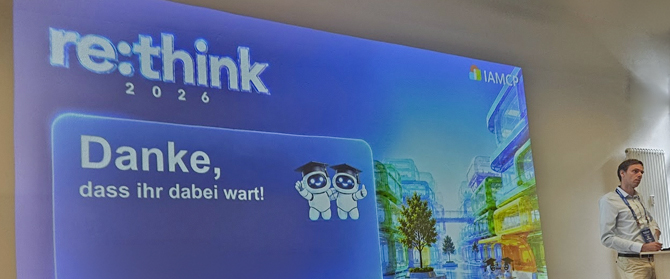 Ein Mann steht bei einer Konferenz oder Präsentation vor einer Leinwand, auf der „re:think 2026“ und „Danke, dass ihr dabei wart!“ zu lesen sind, begleitet von Comic-Robotern und futuristischen Stadtgrafiken.