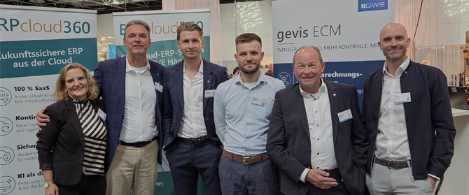 Fünf Personen stehen in einer Reihe an einem Messestand vor Firmenbannern.